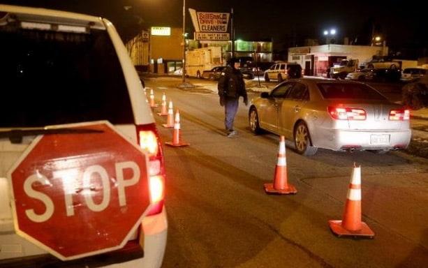Nighttime view of Mississippi DUI roadblock with stop sign, traffic cones, and stopped cars.